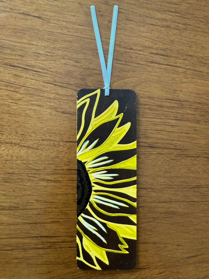 Black bookmark with yellow sunflower design on a wooden surface