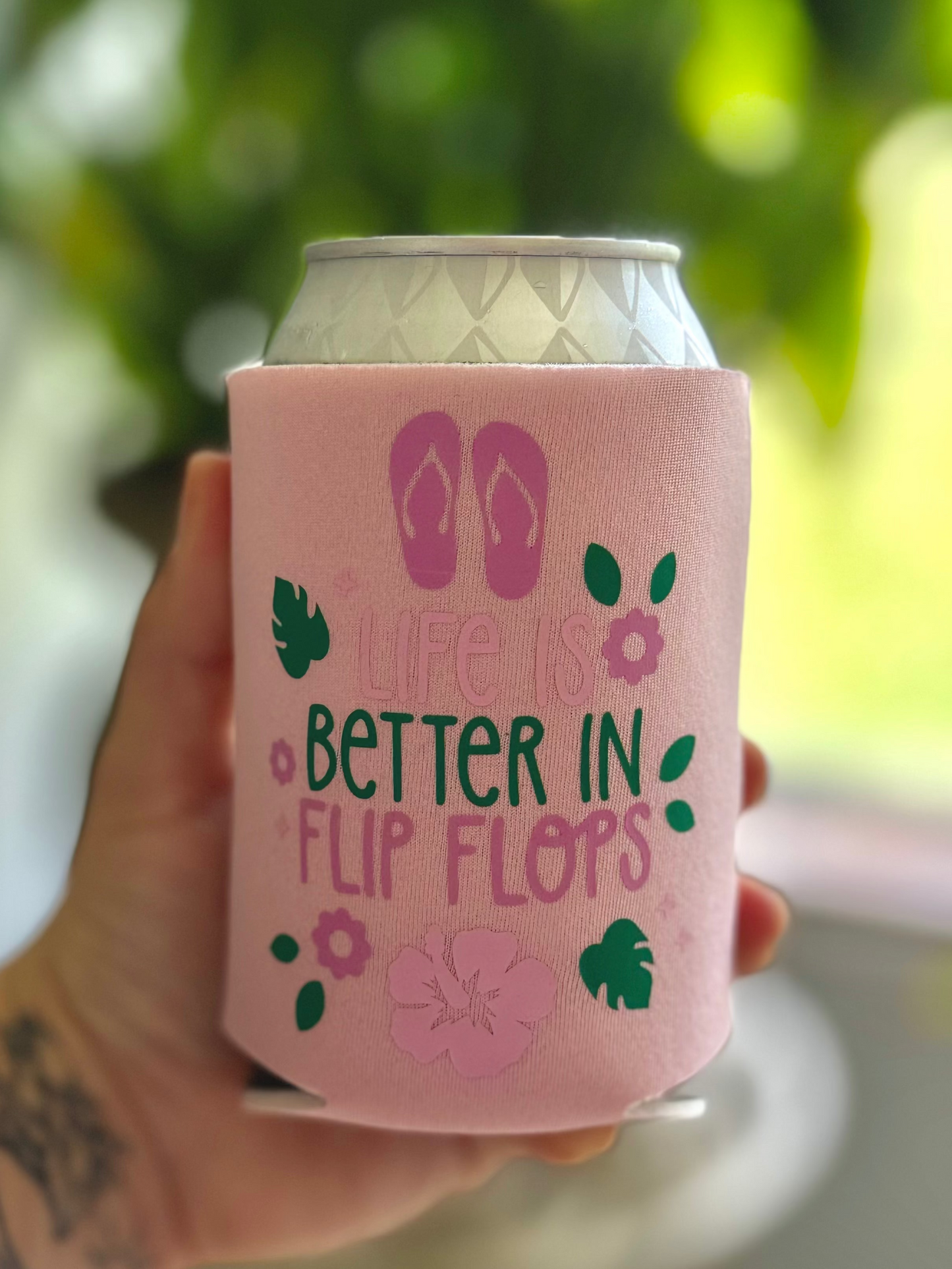 Pink can cooler with 'Life is better in flip flops' text held by a person.