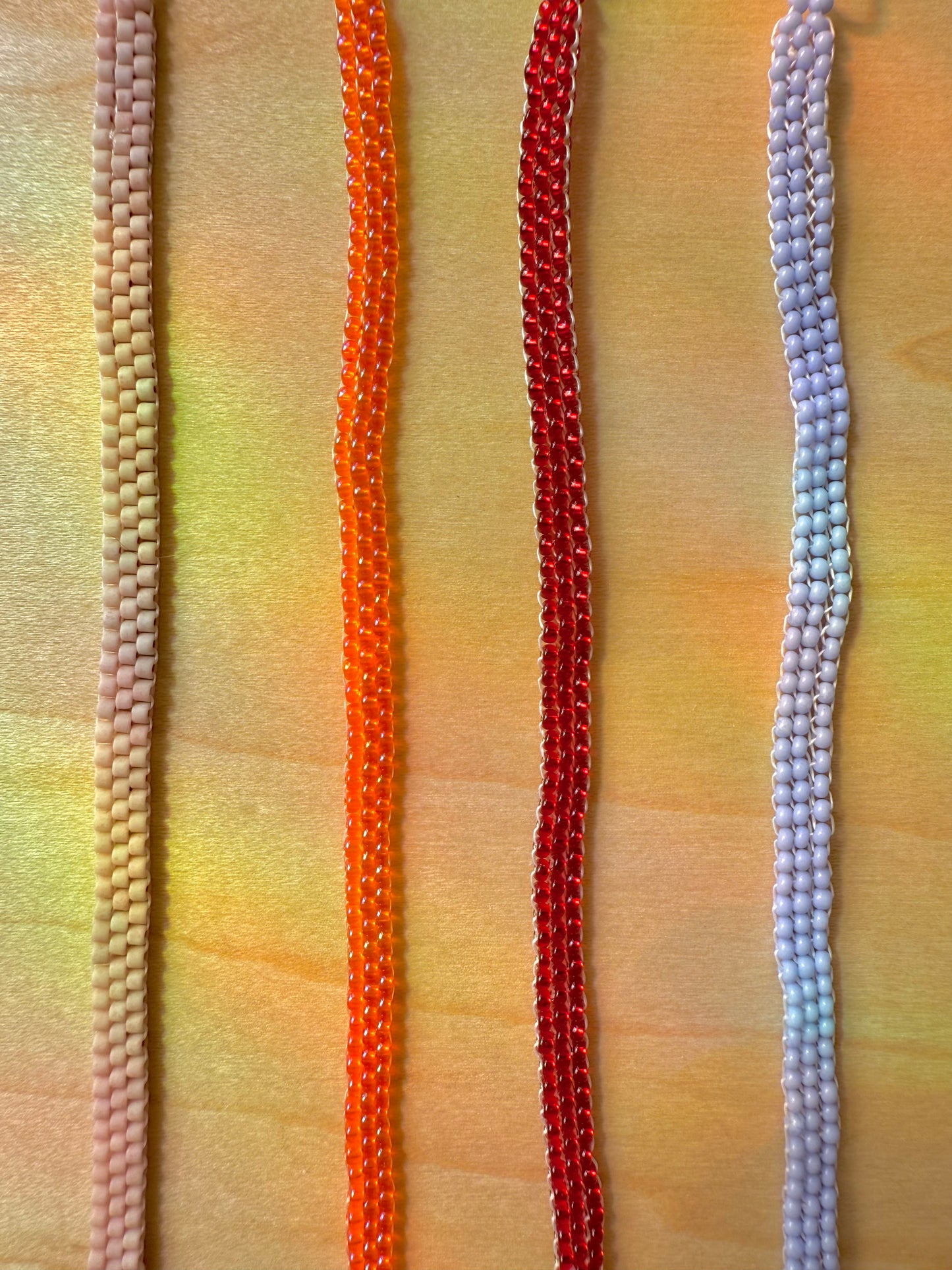Four colorful beaded necklaces on a textured fabric background