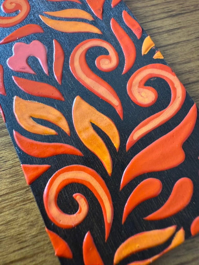 Close-up of a decorative bookmark with orange and pink patterns on a wooden surface