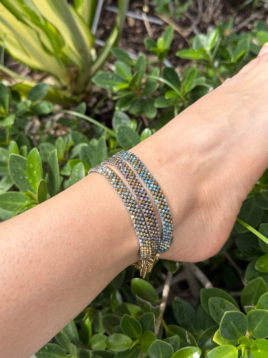 Person's wrist wearing a beaded bracelet with greenery in the background