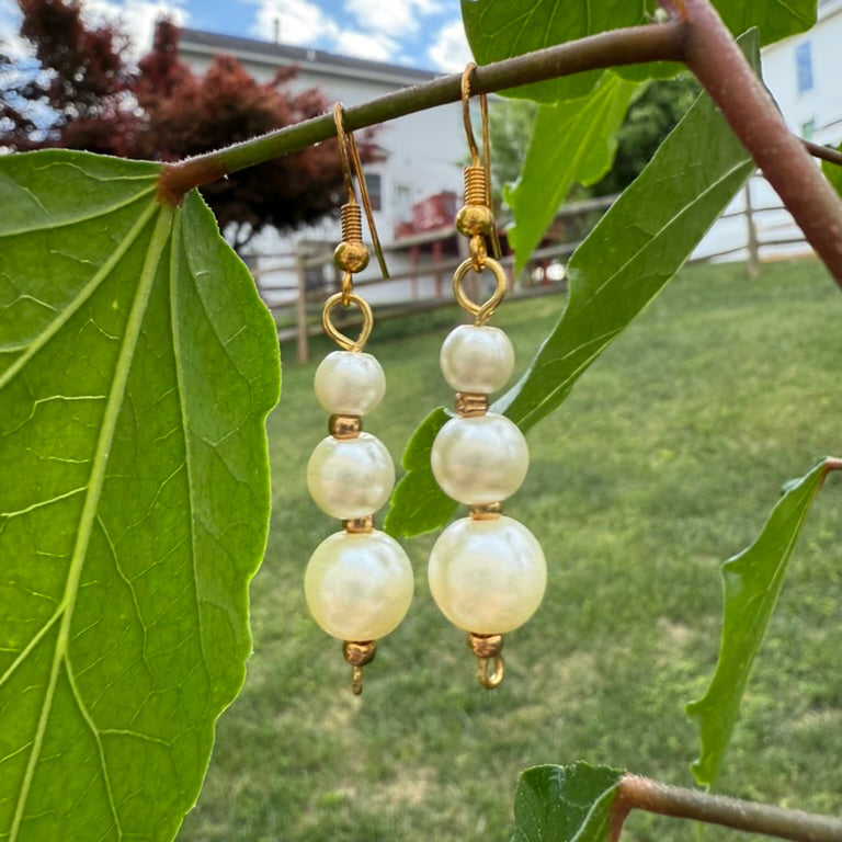 Pearl earrings hanging from a branch with green leaves in the background