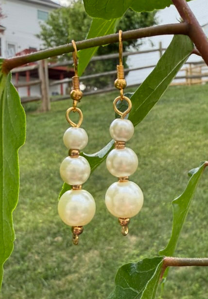 Pearl earrings hanging from a branch with green leaves and a blurred outdoor background