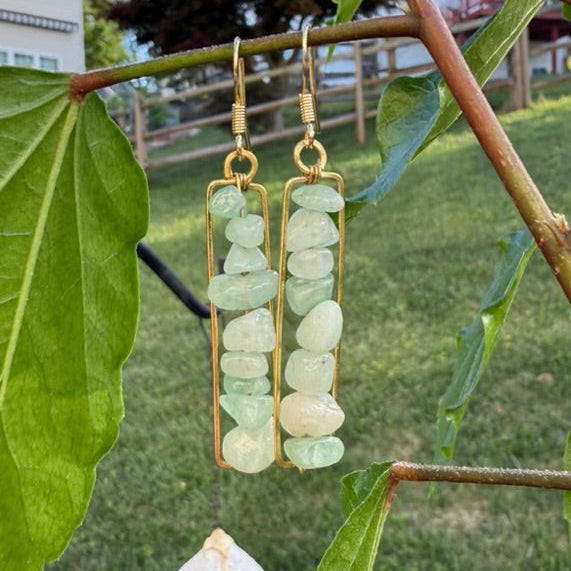 Green stone earrings hanging from a branch with leaves in the background