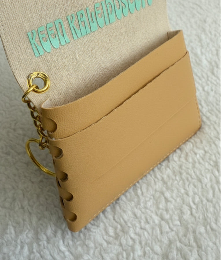 Small beige leather pouch with gold chain and decorative text on a textured surface