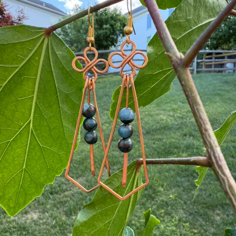 Copper earrings with black beads hanging on green leaves outdoors