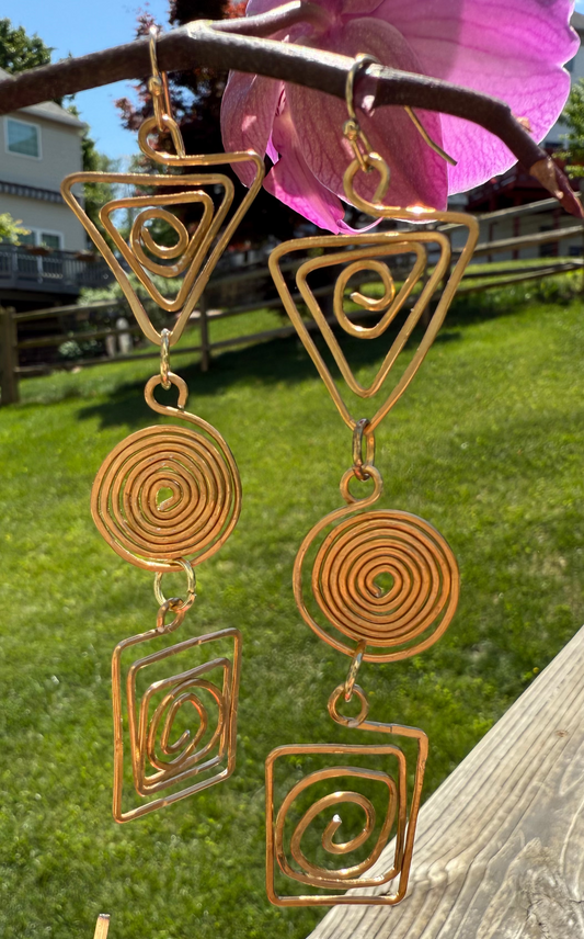 Decorative earrings with geometric designs hanging from a branch outdoors.