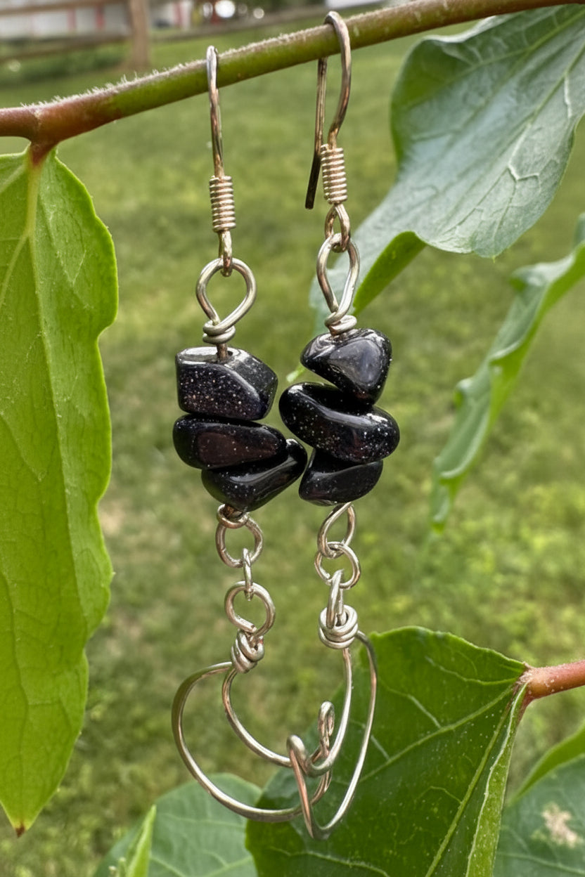 Black stone earrings with silver hooks on a branch with green leaves