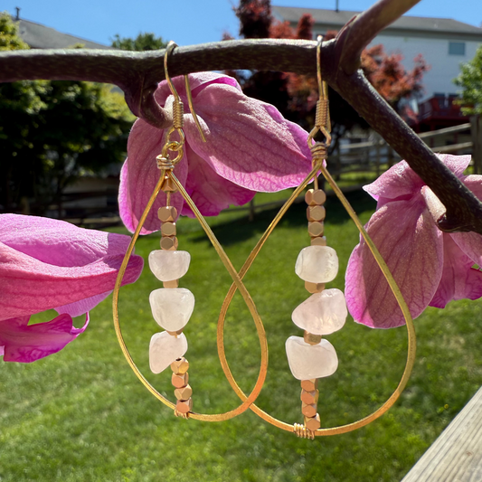 Gold hoop earrings with pink stones hanging on a branch with pink flowers.