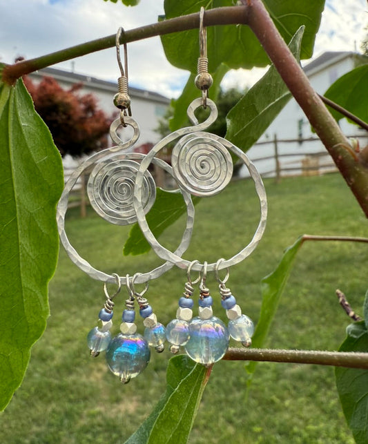 Silver spiral earrings with glass beads hanging on a branch with leaves.