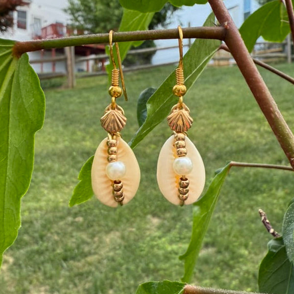 Gold earrings with pearl-like beads hanging from a branch with green leaves.
