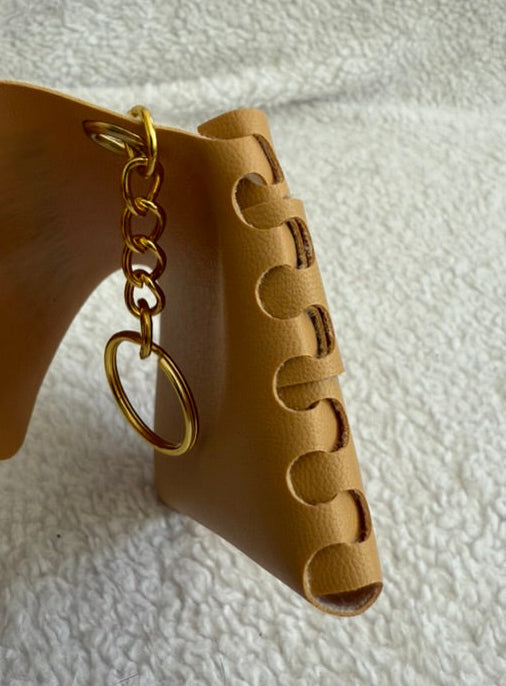 Beige leather keychain with gold ring held by a hand on a textured white surface