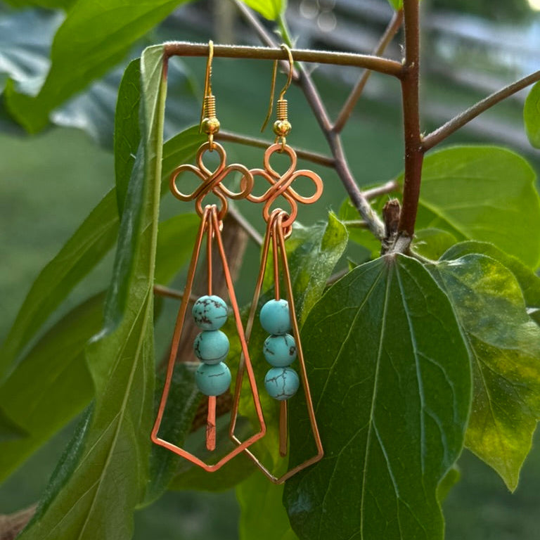 Copper earrings with turquoise beads hanging on a branch with green leaves.