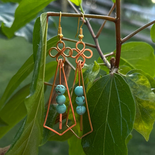 Copper earrings with turquoise beads hanging on a branch with green leaves.