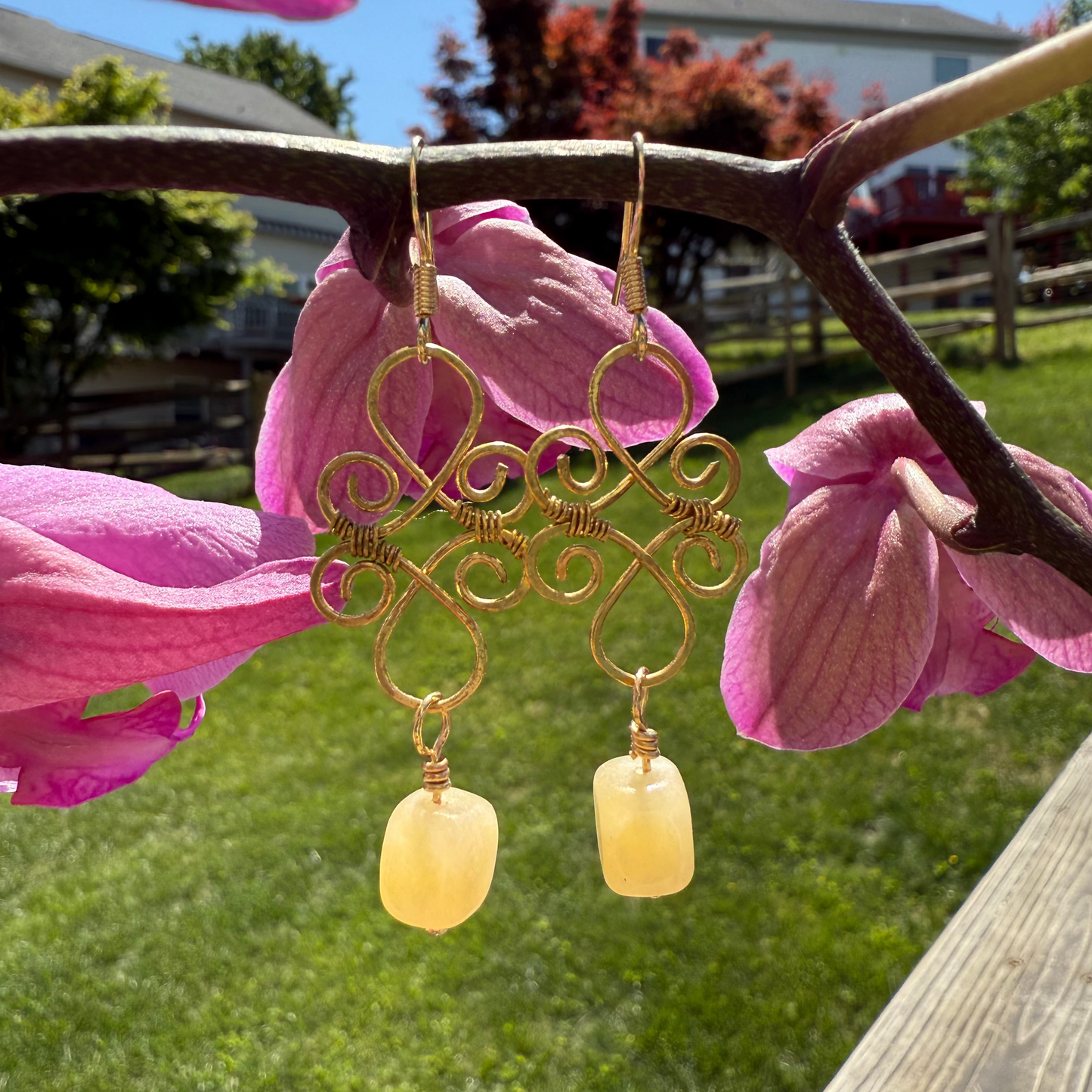 Gold earrings with yellow beads hanging from pink flowers outdoors.