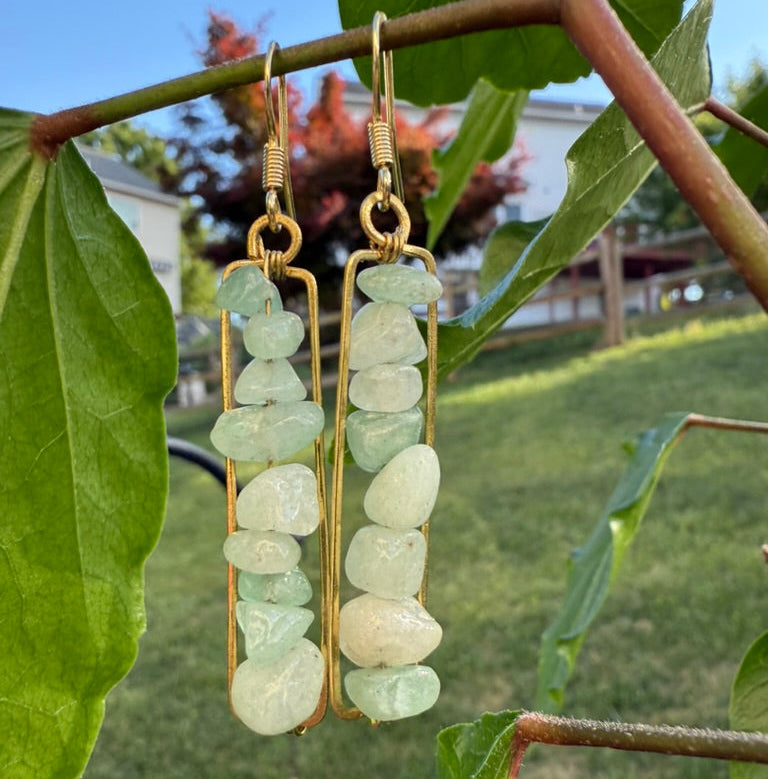 Green stone earrings on a branch with a blurred outdoor background